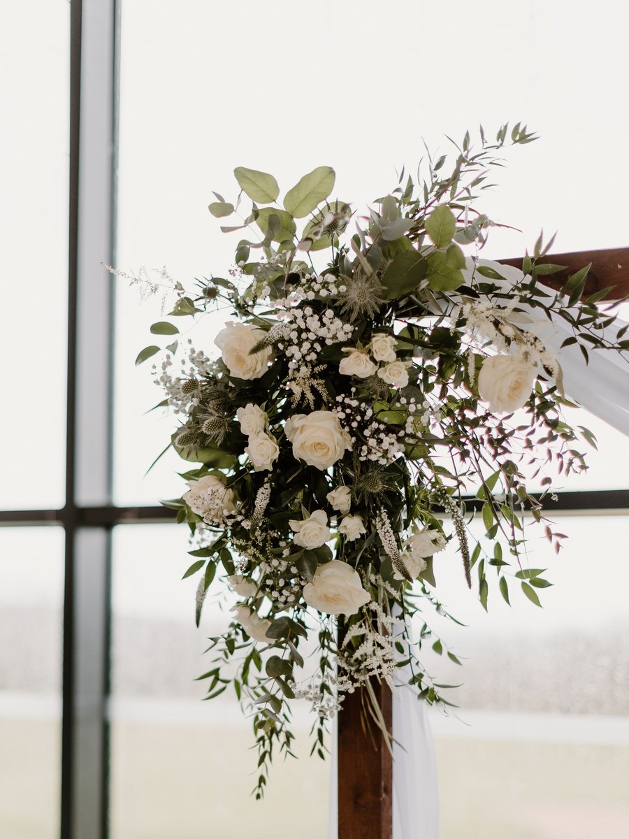 Licensed stock photograph: white roses, gypsophila and trailing greenery gathered at the corner of a wooden ceremony arbour with white drapery.