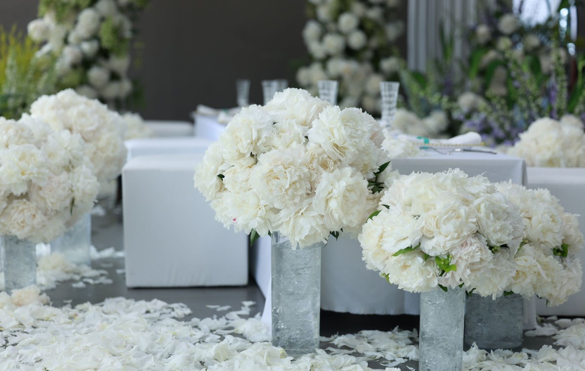 Licensed stock photograph: cylinder vases of white peonies set along an aisle of scattered petals, with a floral backdrop behind.