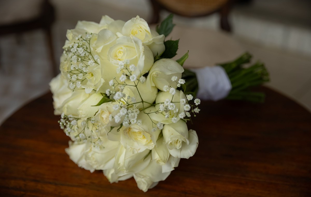 Licensed stock photograph: a bridal bouquet of ivory roses and gypsophila, its stems bound in white ribbon, lying on a polished wooden table.